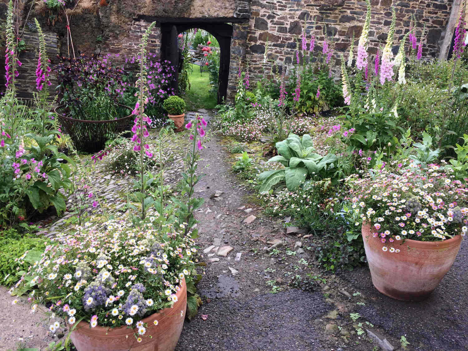 Image showing potted and bedded plants at Frizenham Farmhouse leading to an archway in the background.